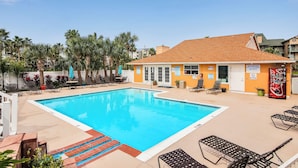 A rectangular swimming pool with a tiled deck, surrounded by lounge chairs and palm trees. - Glowing Fun by Ryson Vacation Rentals (Galveston)