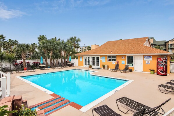 A rectangular swimming pool with a tiled deck, surrounded by lounge chairs and palm trees. - Glowing Fun by Ryson Vacation Rentals (Galveston)