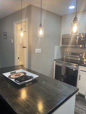 A kitchen with a dark countertop, stainless steel appliances, pendant lighting, and a door with a light switch. - High Plains Lodge at Nomad Landing (Clayton)