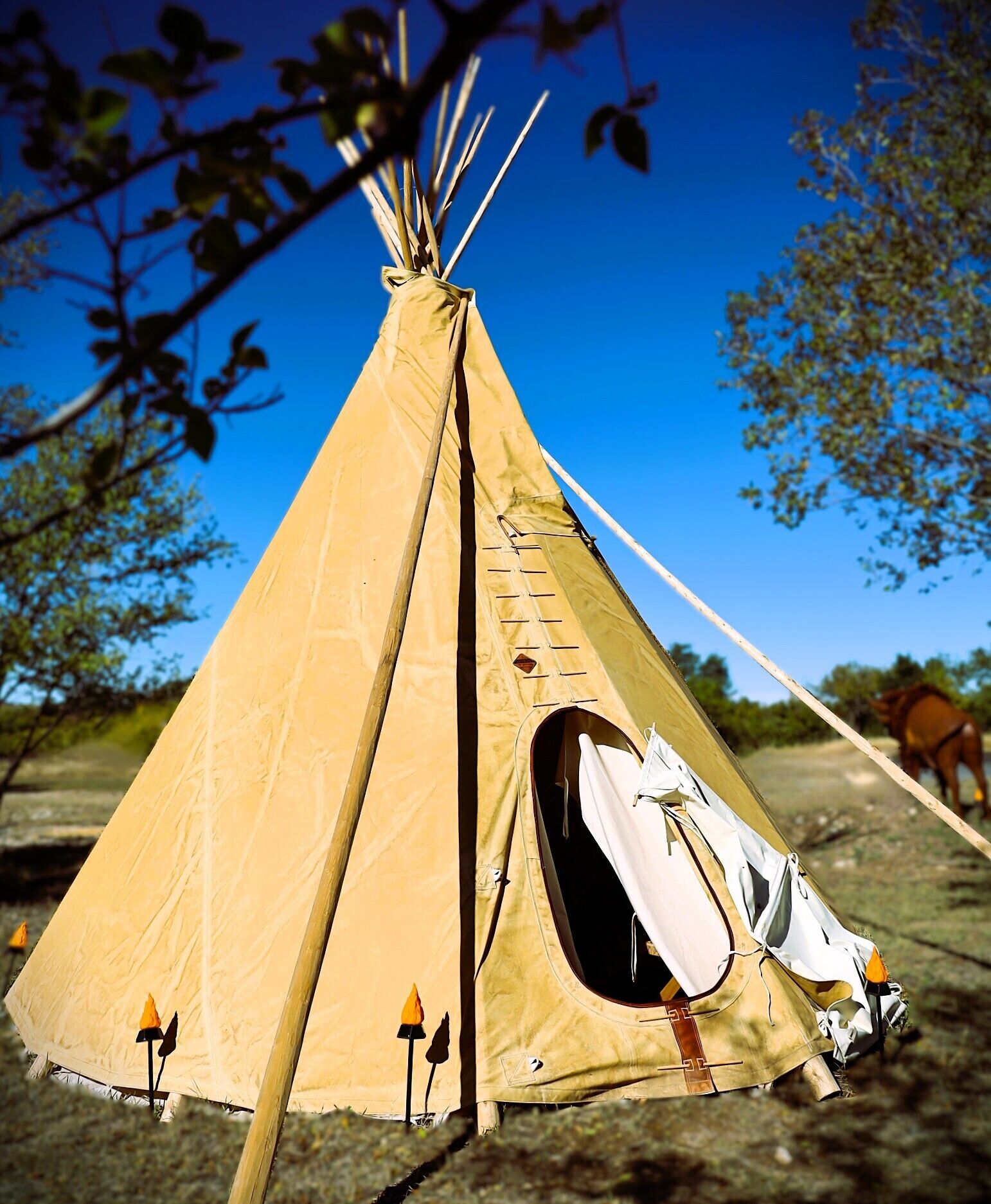 A traditional conical tent with a canvas exterior, a central entrance, and a small attached structure with a white covering.