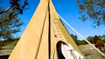 A traditional conical tent with a canvas exterior, a central entrance, and a small attached structure with a white covering.
