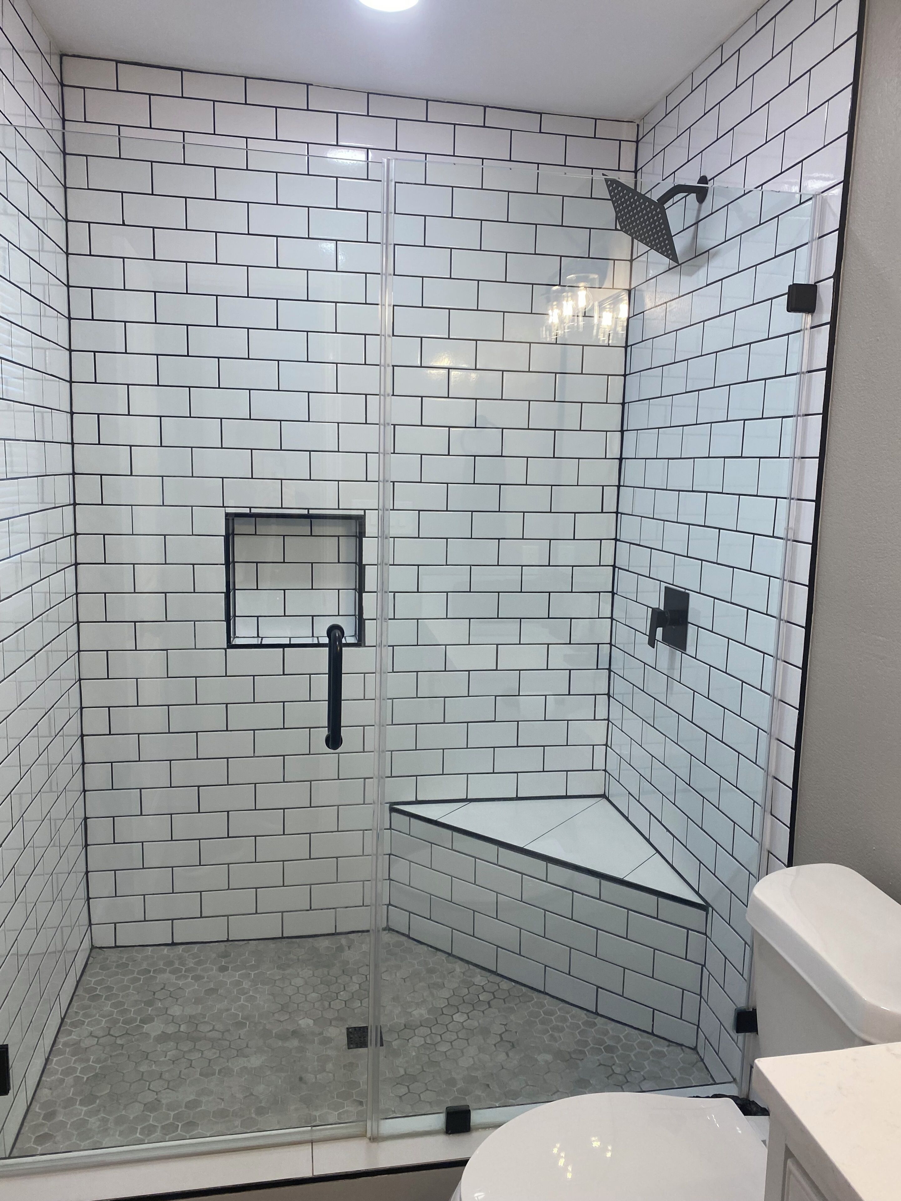 A shower with a glass door, white tiled walls, and a hexagonal floor pattern.