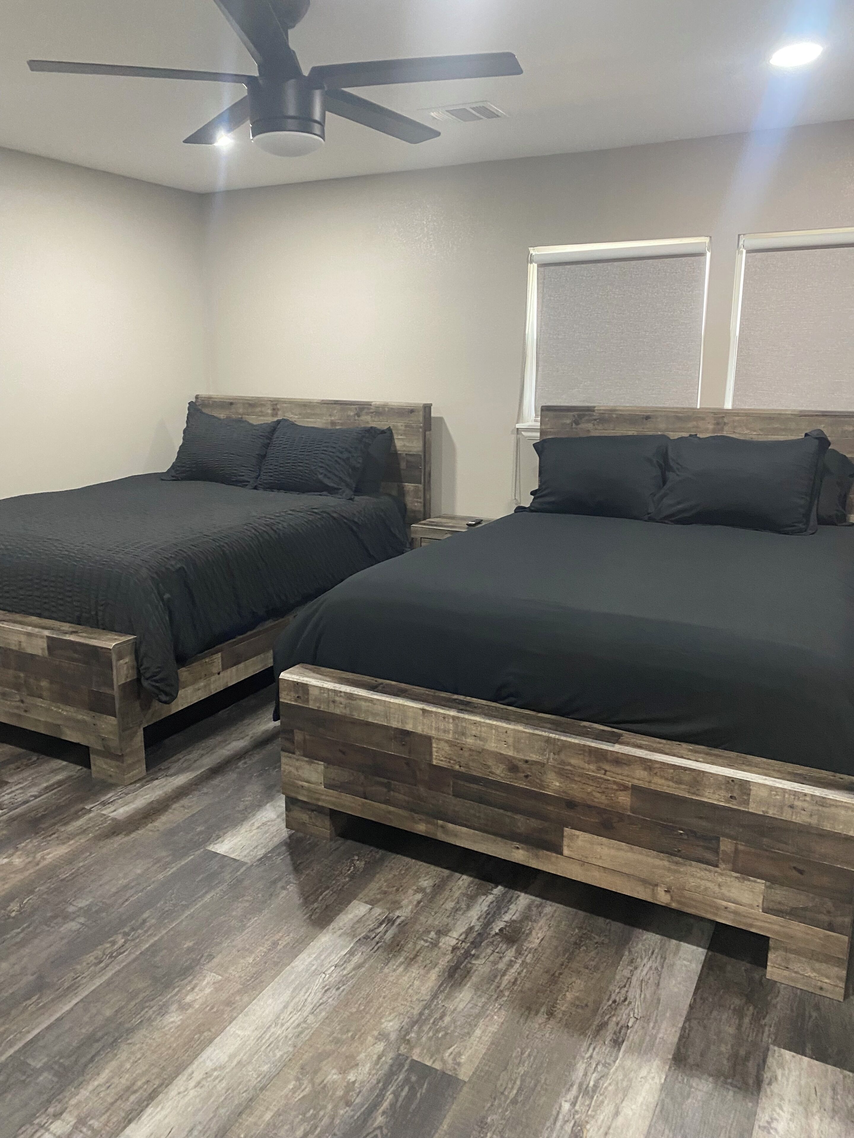 Two wooden beds with dark bedding in a room with a wooden floor and a ceiling fan.