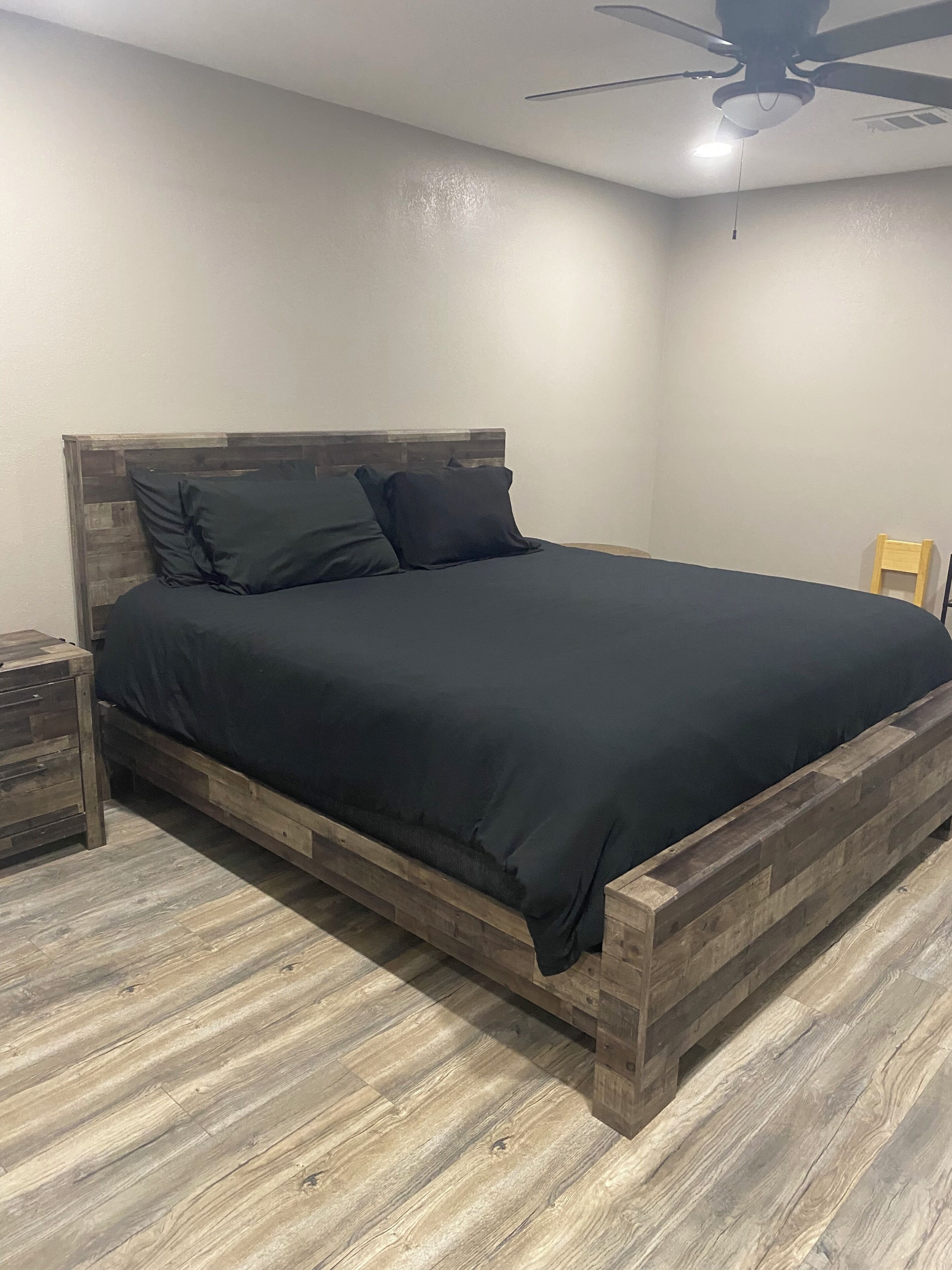 A bedroom with a wooden bed frame, a nightstand, and a ceiling fan.