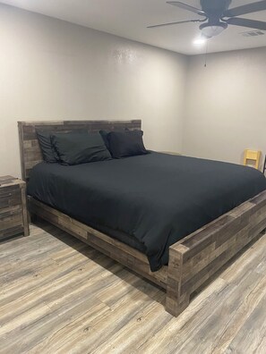 A bedroom with a wooden bed frame, a nightstand, and a ceiling fan. - High Plains Lodge at Nomad Landing (Clayton)