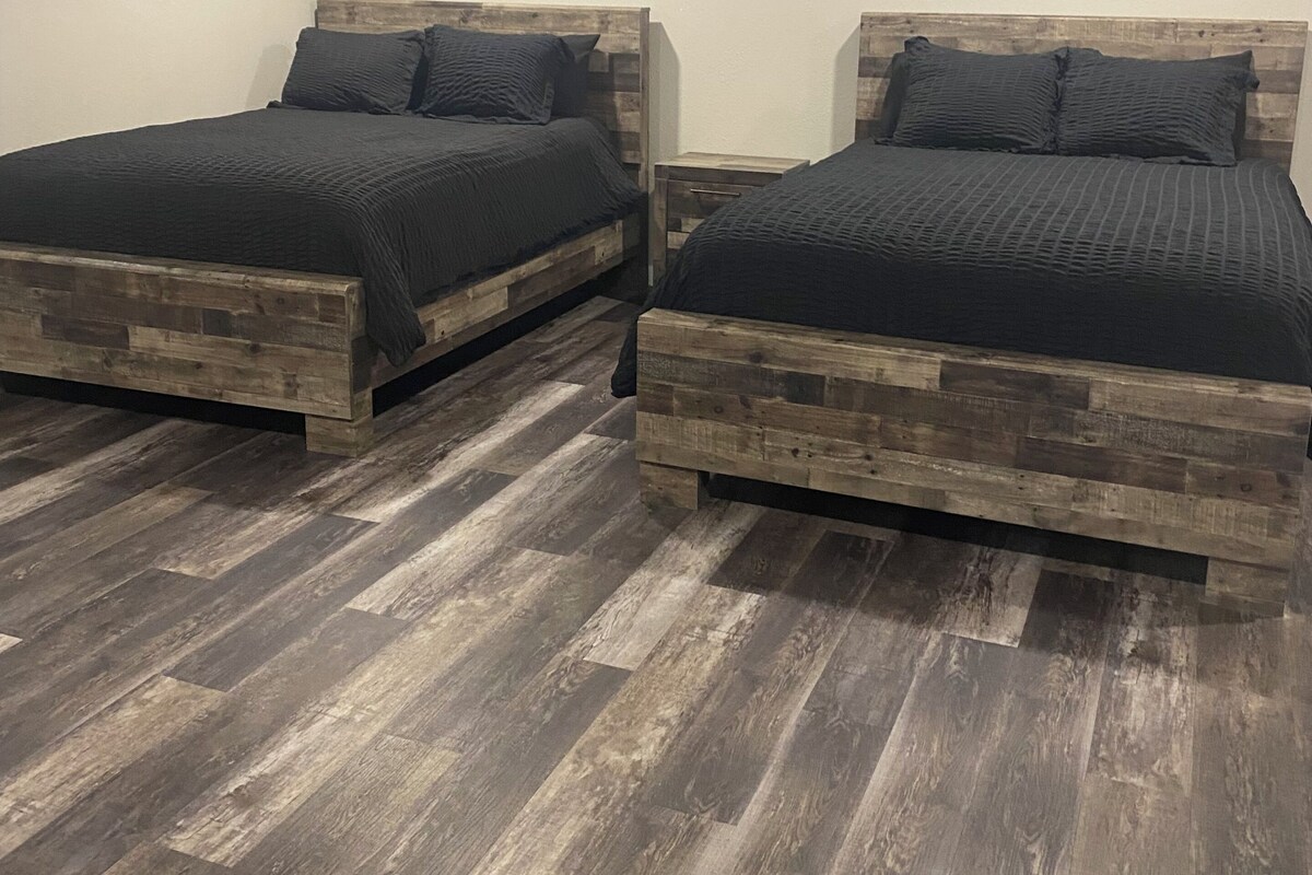 Two wooden beds with dark bedding in a room with wooden flooring and a ceiling fan.