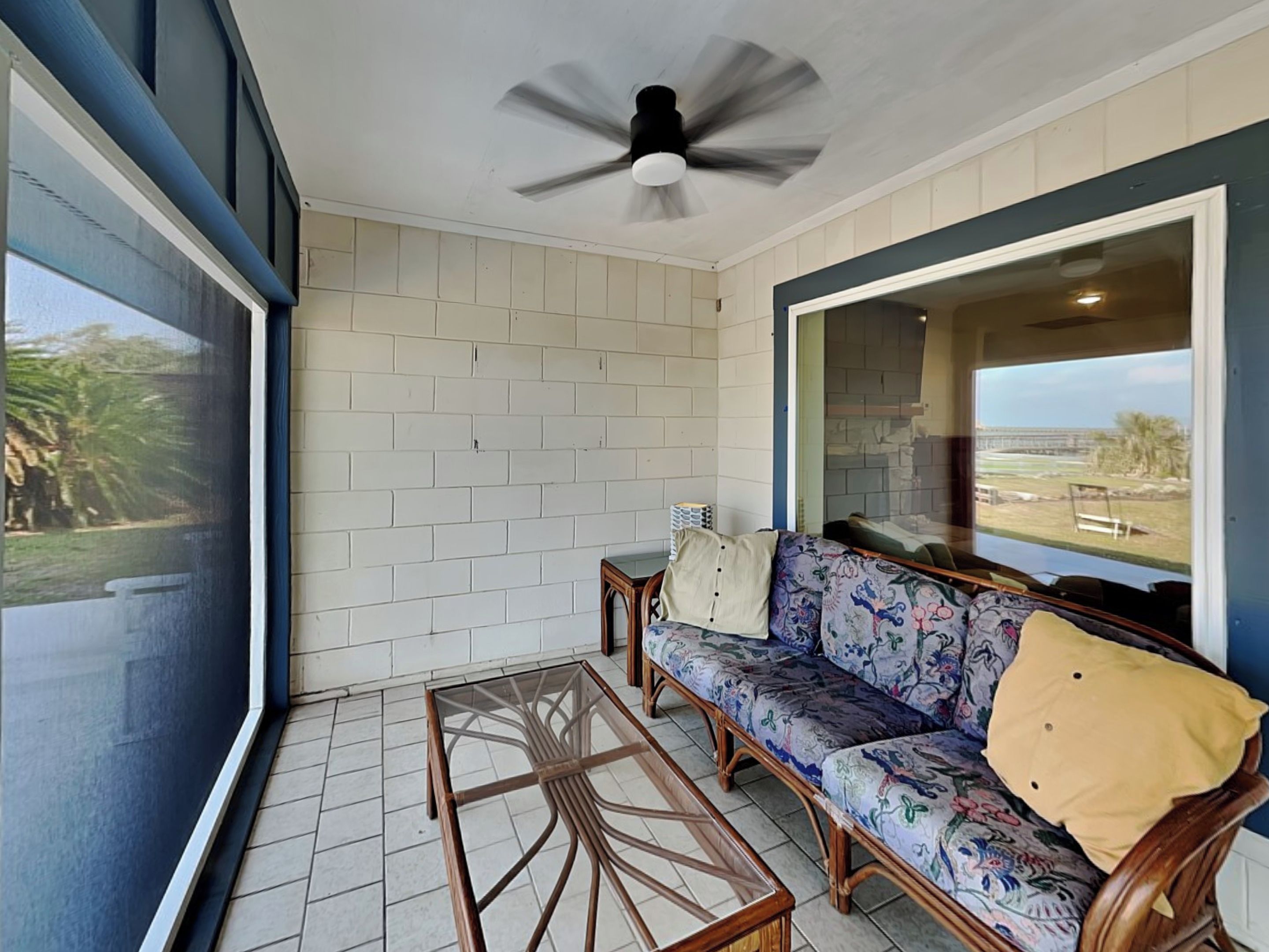 Una habitación con una mesa de centro de vidrio, un sofá con tapicería floral y vista a una playa a través de un ventanal grande.
