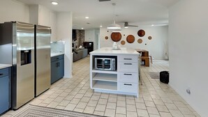 Eine moderne Küche mit Edelstahlgeräten, einer weißen Kücheninsel mit Mikrowelle sowie einem Essbereich mit Holztisch und -stühlen.
