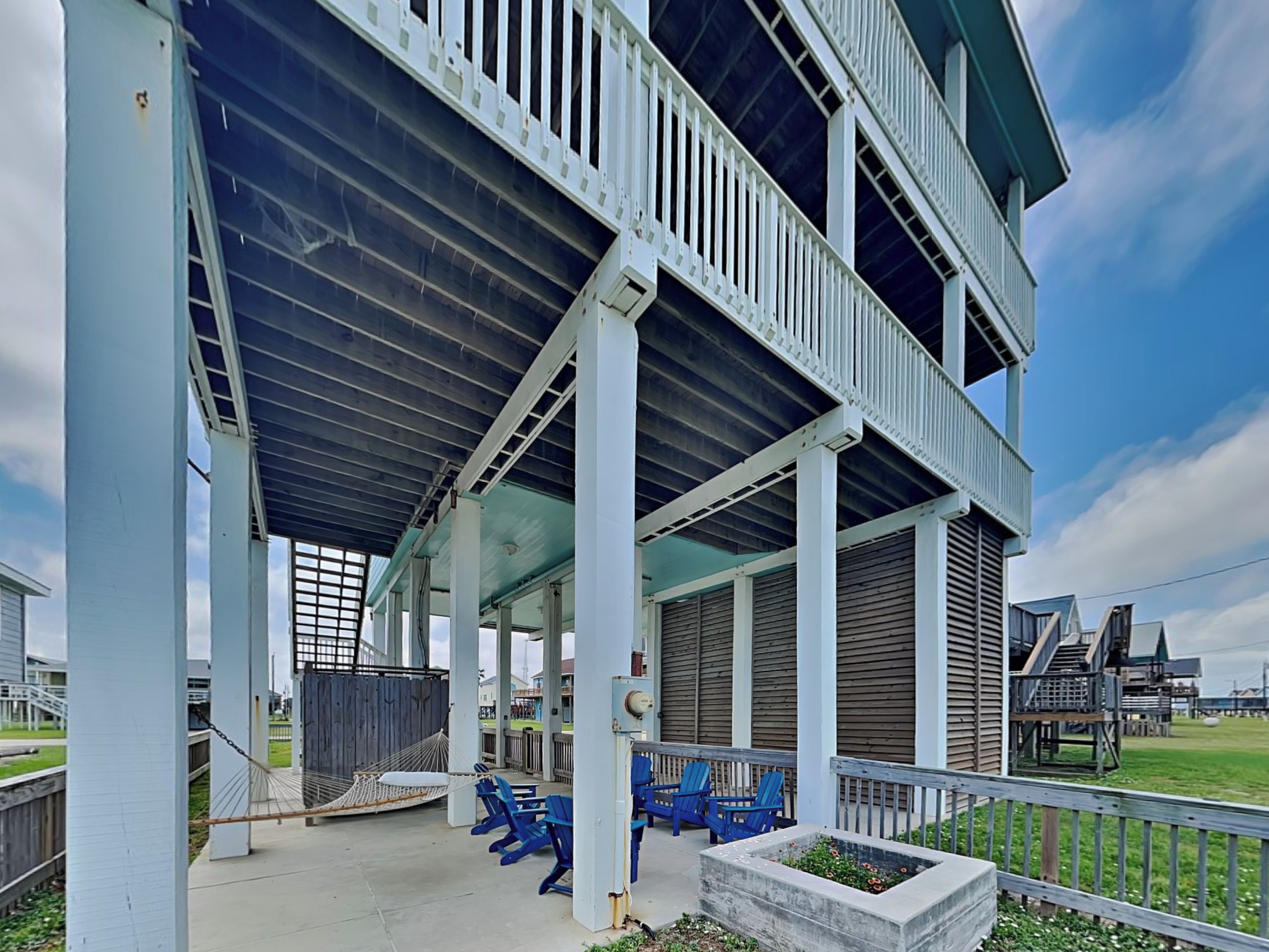A covered outdoor area with blue chairs and a hammock, supported by white columns.