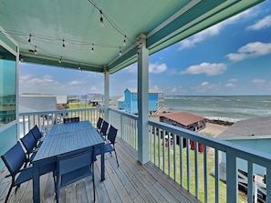 A covered outdoor deck with a table and chairs, overlooking a beach with houses and the ocean. - Sea Forever by Ryson Vacation Rentals (Freeport)