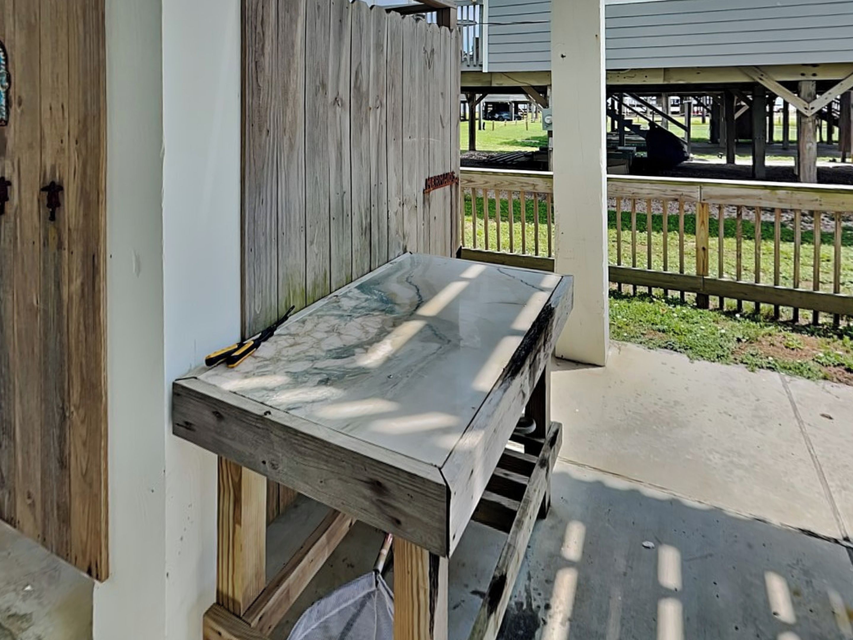 A wooden table with a marble top, positioned under a porch with a white railing.