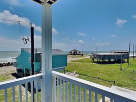 Vista costera desde un balcón con barandilla, con vista a un área verde y un edificio junto a la playa.