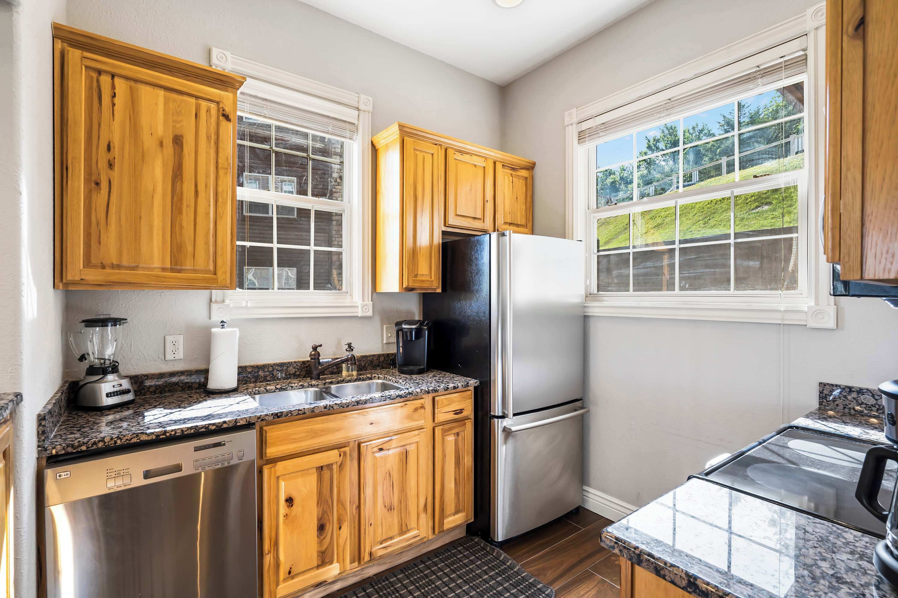 A kitchen with wooden cabinets, a stainless steel refrigerator, a dishwasher, and a granite countertop.