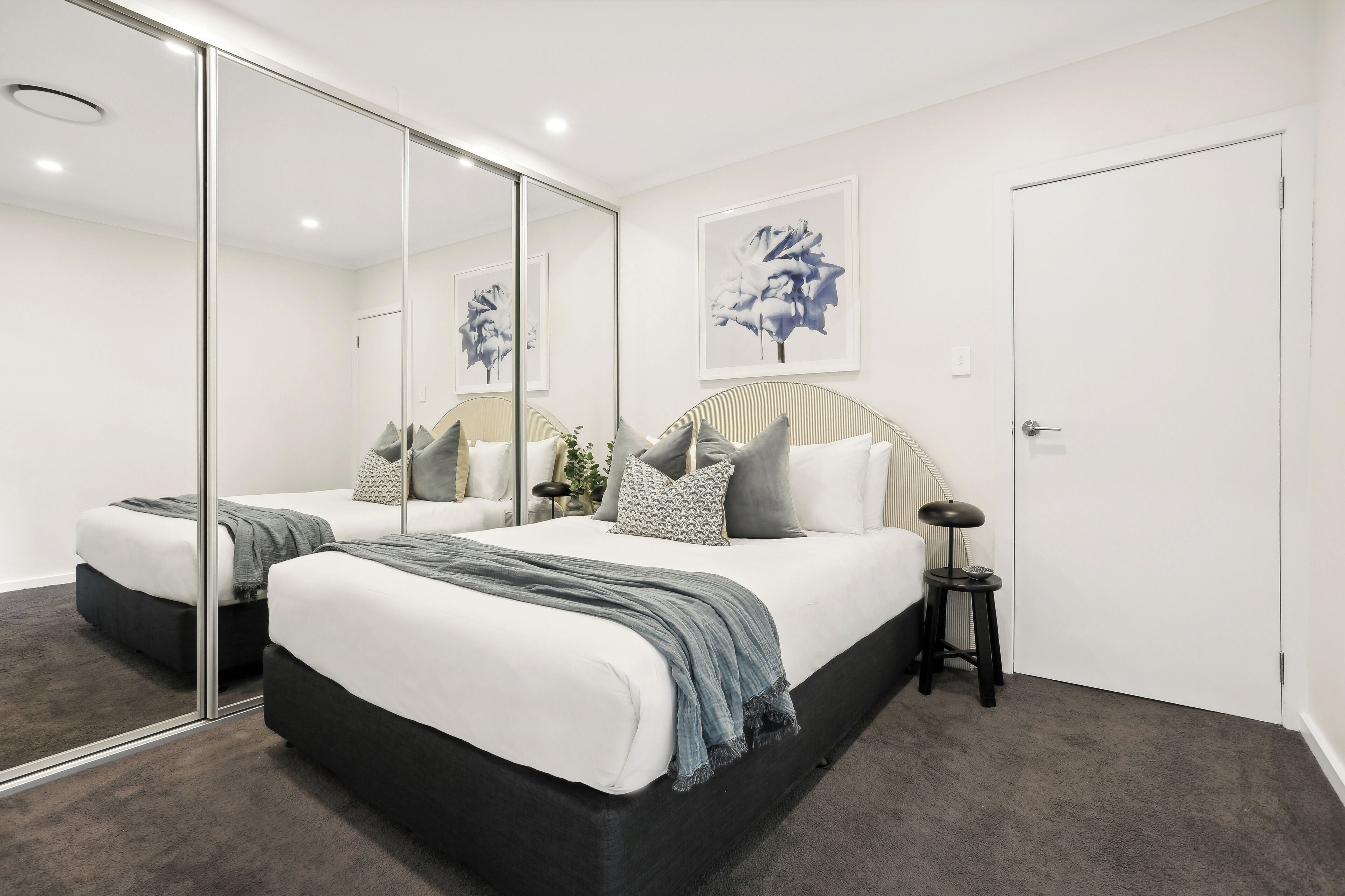 A modern bedroom with a large bed, a bedside table, a mirror, and a framed artwork on the wall.