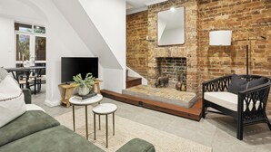 Un salon moderne avec une cheminée en briques, un fauteuil en osier noir et un canapé vert.