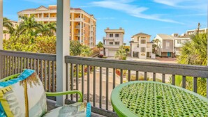 A balcony with a green chair and a white cushion, overlooking a residential area with various buildings and palm trees. - Sunshine Lane by Distinctive Beach Rentals (Treasure Island)