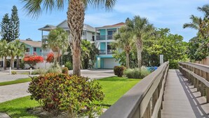 A resort with a wooden boardwalk, palm trees, and a building with balconies. - Sunshine Lane by Distinctive Beach Rentals (Treasure Island)
