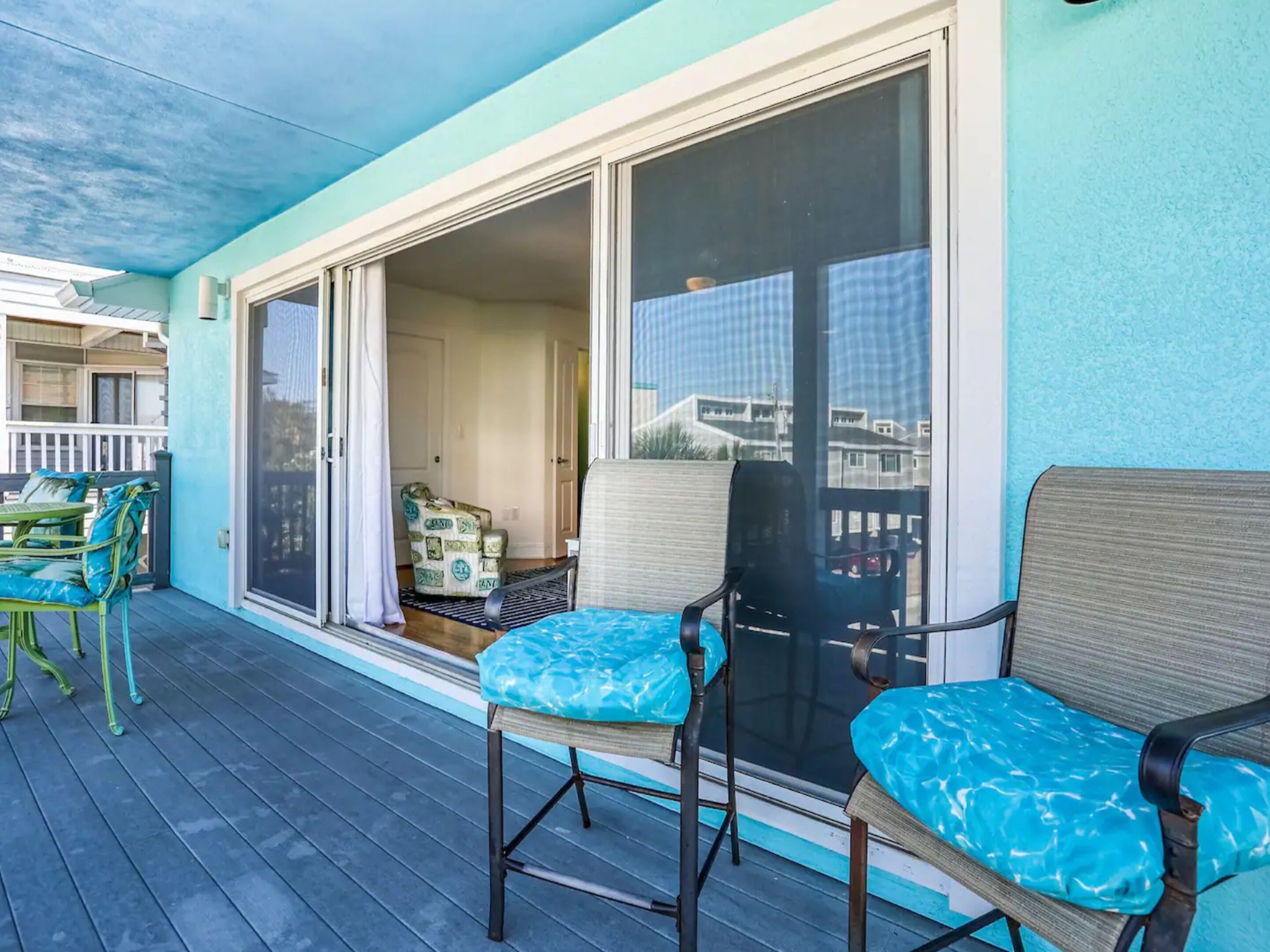 A covered outdoor area with a pool table, two chairs with blue cushions, and a sliding glass door leading to an indoor space.