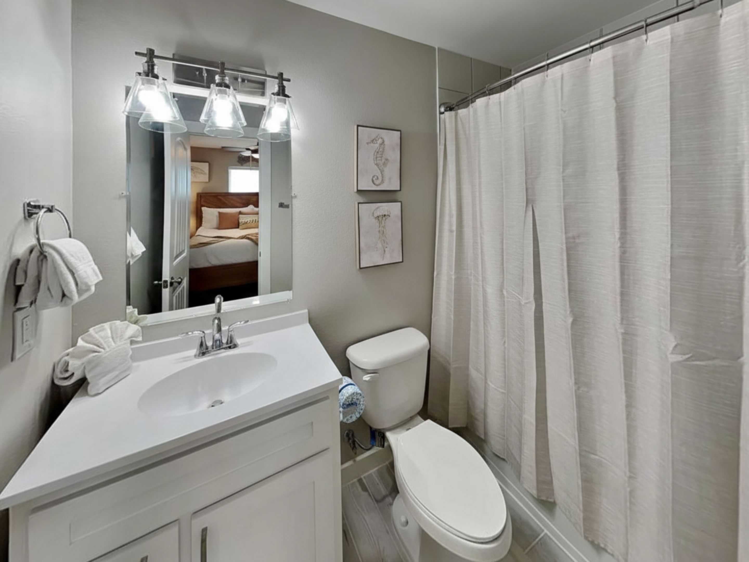 A bathroom with a white sink, mirror, and toilet. There is a shower curtain and towels on the wall.