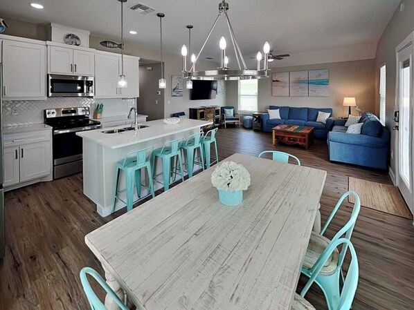 A modern kitchen with white cabinets, stainless steel appliances, and a central island with bar stools. - The Blue Heron by Silver Sands Vacation Rentals (Port Aransas)