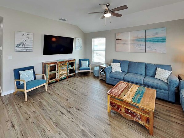 A living room with a blue sofa, two blue armchairs, a wooden coffee table, and a ceiling fan. - The Blue Heron by Silver Sands Vacation Rentals (Port Aransas)