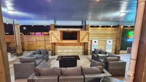 An outdoor seating area with wicker furniture and a flat-screen TV mounted on a wooden wall. - The Blue Heron by Silver Sands Vacation Rentals (Port Aransas)