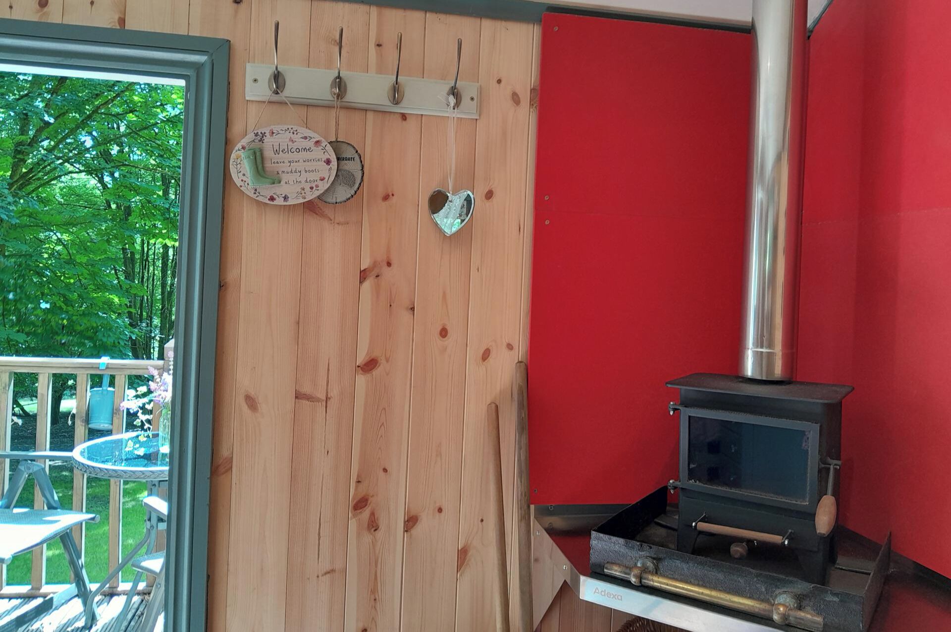 A wooden interior with a red wall, a metal stove, and a door with a welcome sign.