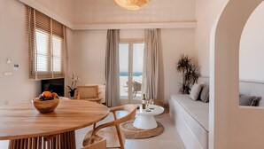 A modern living room with a round wooden dining table, a white sofa, and a view of the sea through a large window. - Halo Santorini- Living Experience (Santorini)
