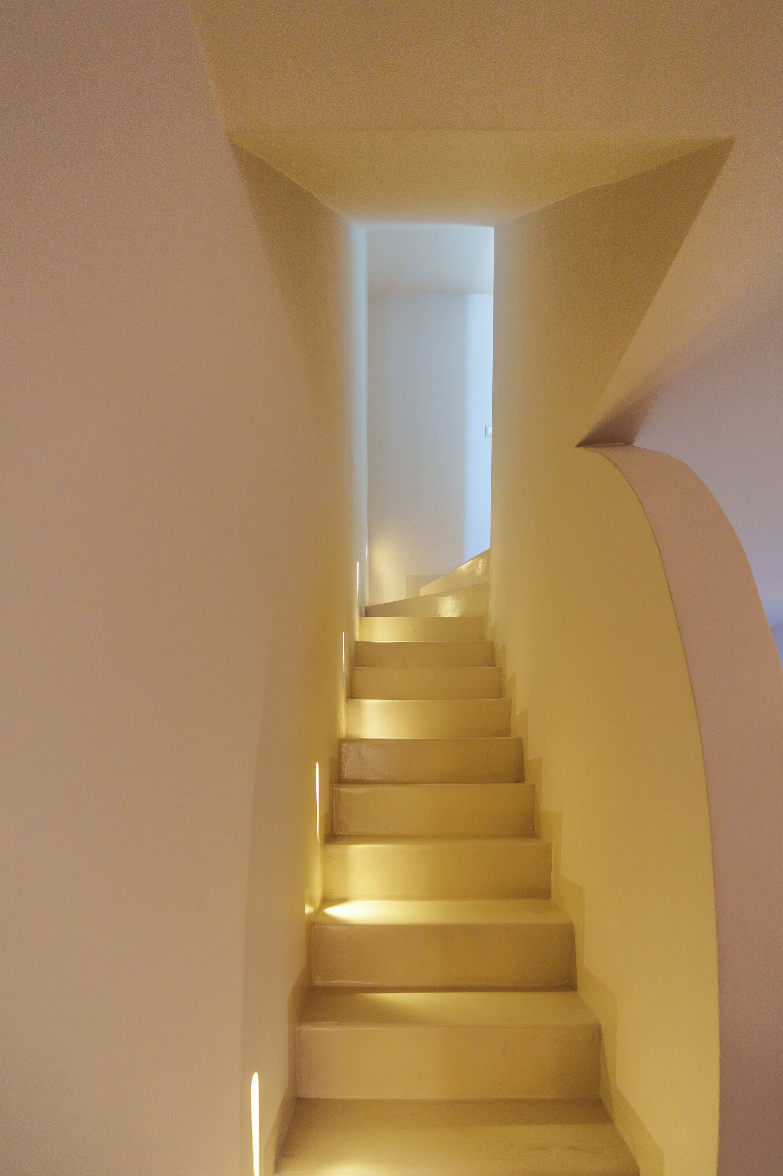 A staircase with a curved wall on one side and a straight wall on the other, leading to a bright room at the top.