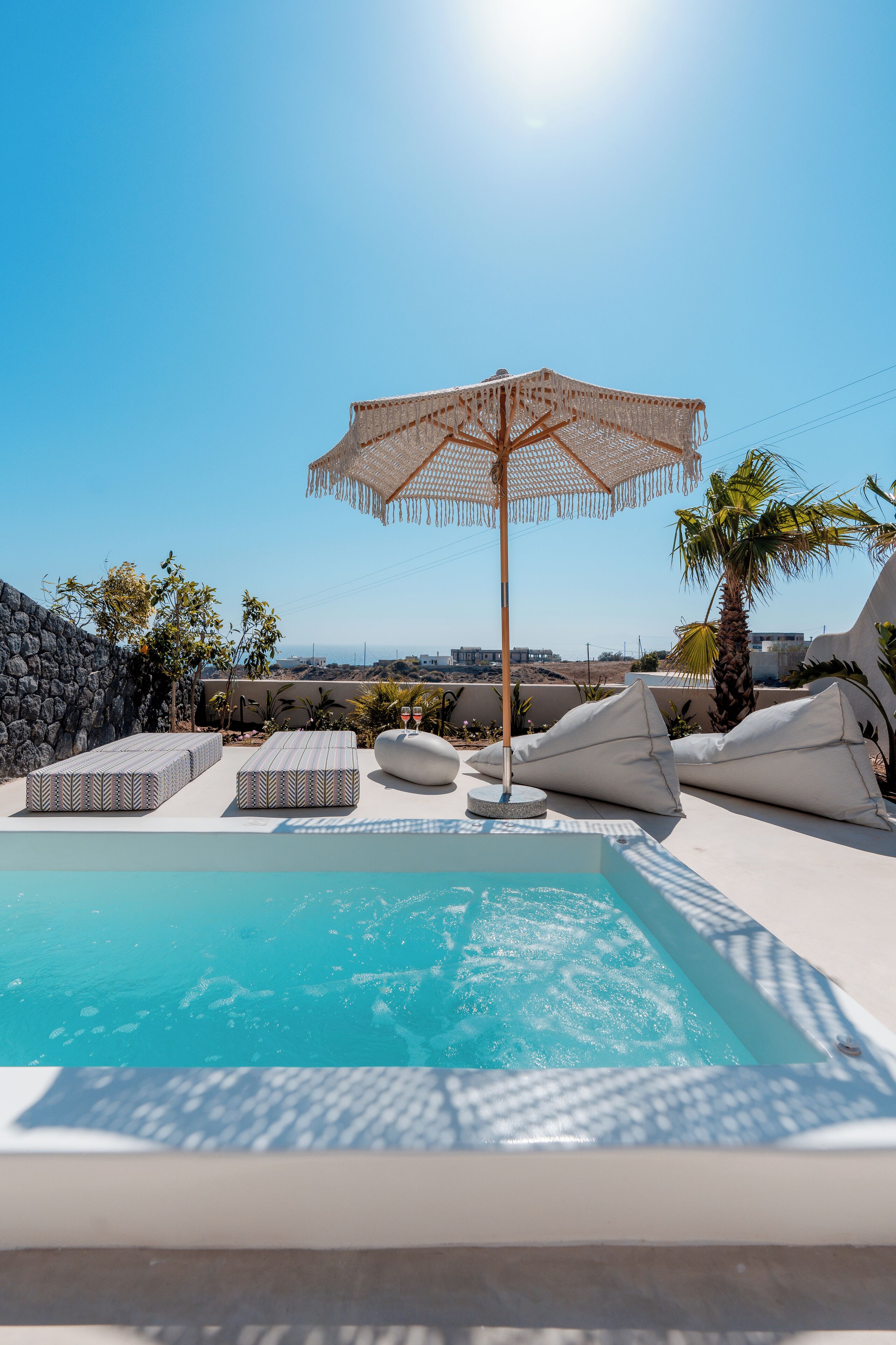 A pool area with lounge chairs, a palm tree, and a clear sky.
