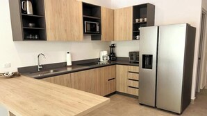 Une cuisine moderne avec des meubles en bois, un réfrigérateur en acier inoxydable, une machine à café et un four à micro-ondes.
