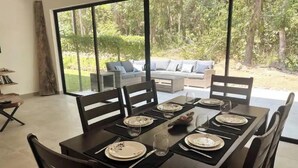 Un coin repas avec une table dressée pour six personnes, de grandes fenêtres et une vue sur un jardin.