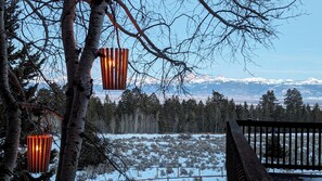 A snowy landscape with a wooden bench and hanging lanterns, overlooking a forest and distant mountains. - Fisherman's Paradise in the Gorgeous Teton Valley (Tetonia)