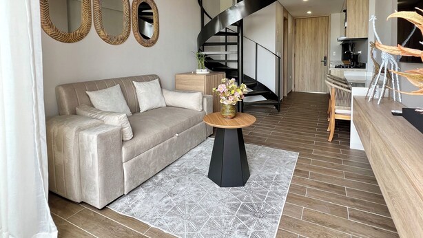 Ett rymligt vardagsrum med en modern trappa, en soffa, ett soffbord och en matplats med stolar.