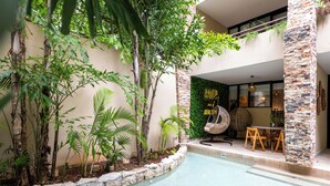 A pool area with a stone border, surrounded by various plants and trees. There is a seating area with a fan and a table. - Studio with Roof Pool Near Beach (Playa del Carmen)