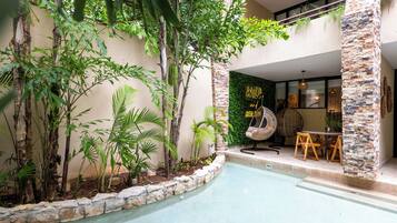 A pool area with a stone border, surrounded by various plants and trees. There is a seating area with a fan and a table.