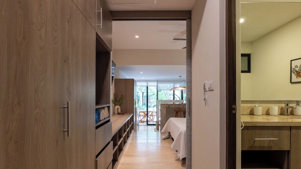 A modern hotel room with a wooden wardrobe, a bed with a white bedspread, a small table with a plant, and a view of the outdoors through a glass door. - Studio with Roof Pool Near Beach (Playa del Carmen)