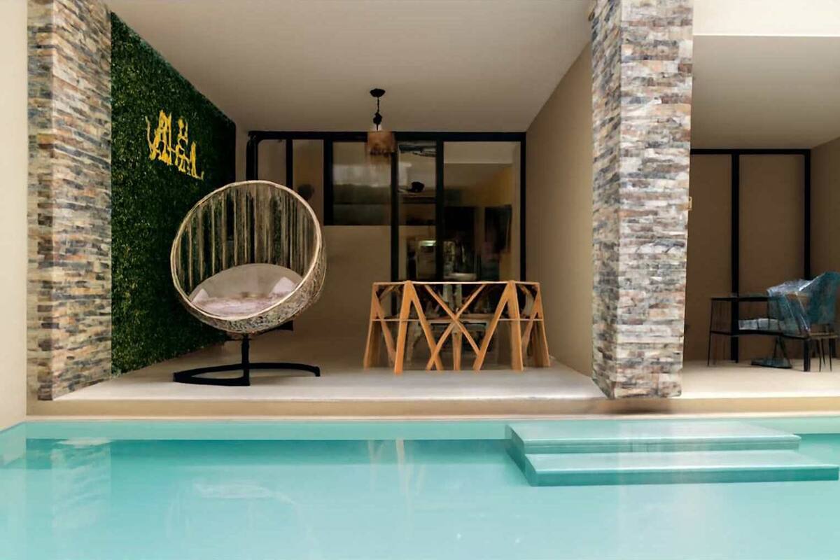 Area piscina moderna all'aperto con una poltrona da relax, un tavolo in legno e un muro in pietra con insegna dorata.