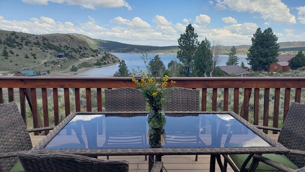 A deck with wicker chairs and a glass table, overlooking a lake and hills. - Charming Lakeview Cabin at Panguitch Lake (Panguitch)