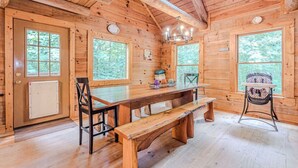 Interior de una cabaña de madera con una gran mesa de comedor, bancos y un techo alto.