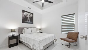 A bedroom with a bed, nightstands, a chair, a ceiling fan, a window with blinds, and a wall-mounted picture.