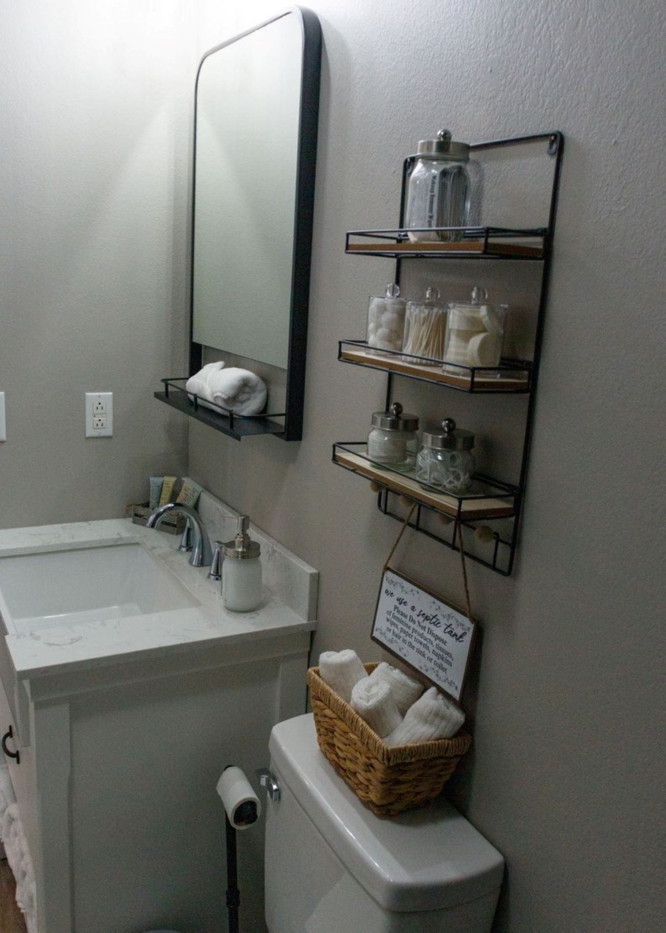 A bathroom with a white sink, mirror, and toilet. There are shelves with toiletries and a basket of towels.