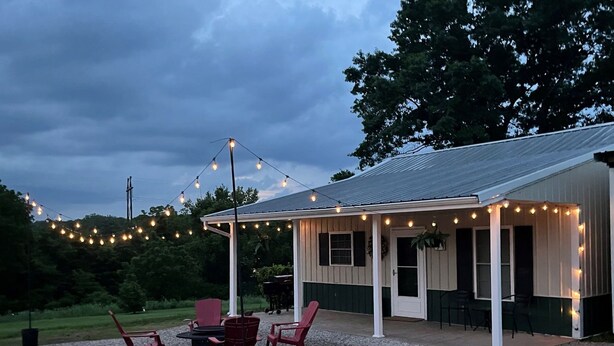 A covered outdoor seating area with a table and chairs, string lights, and a gravel ground. - Clifford's Country Cottage (Bonne Terre)