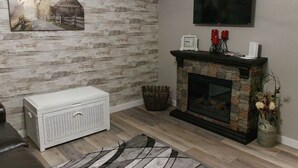 A living room with a rustic wooden wall, a fireplace, a flat-screen TV, and a white sideboard. - Clifford's Country Cottage (Bonne Terre)