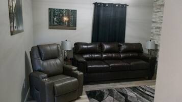 Un salon comprenant un fauteuil en cuir, un canapé en cuir, un tapis et deux lampes fixées au mur.