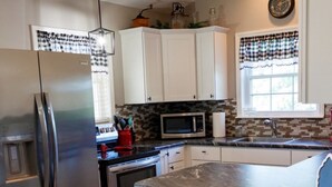 A kitchen with a stainless steel refrigerator, a microwave, and a stone island with two stools. - Clifford's Country Cottage (Bonne Terre)