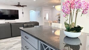 A modern kitchen with a large island, grey cabinetry, and a flat-screen TV mounted above the island. - Posh-Ideal Home Rental for Large Fan Group- WALK to AT&T Stadium- 2 King Beds (Arlington)