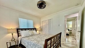 A bedroom with a bed, two bedside lamps, a window with blinds, a door, and a hallway leading to another room. - Posh-Ideal Home Rental for Large Fan Group- WALK to AT&T Stadium- 2 King Beds (Arlington)