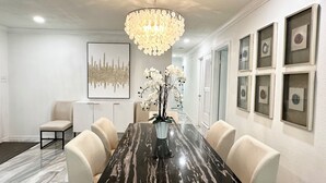 A dining room with a marble table, white chairs, a chandelier, and framed artwork on the walls. - Posh-Ideal Home Rental for Large Fan Group- WALK to AT&T Stadium- 2 King Beds (Arlington)