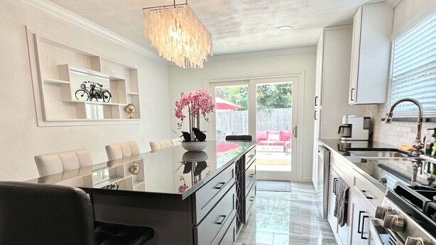 A modern kitchen with a central island, stainless steel appliances, and a dining area with a glass table and chairs. - Posh-Ideal Home Rental for Large Fan Group- WALK to AT&T Stadium- 2 King Beds (Arlington)